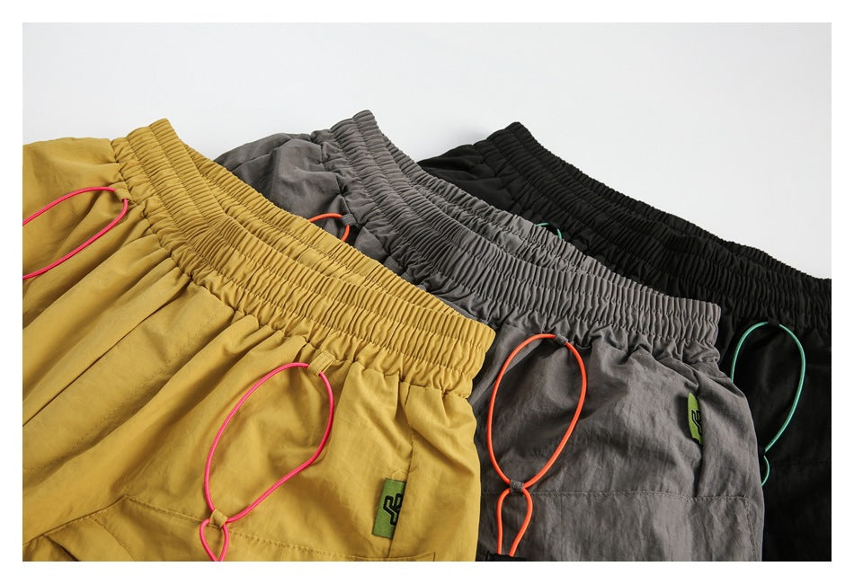 Mustard, gray, and black shorts arranged together, showing gathered waistbands and contrasting drawcords.