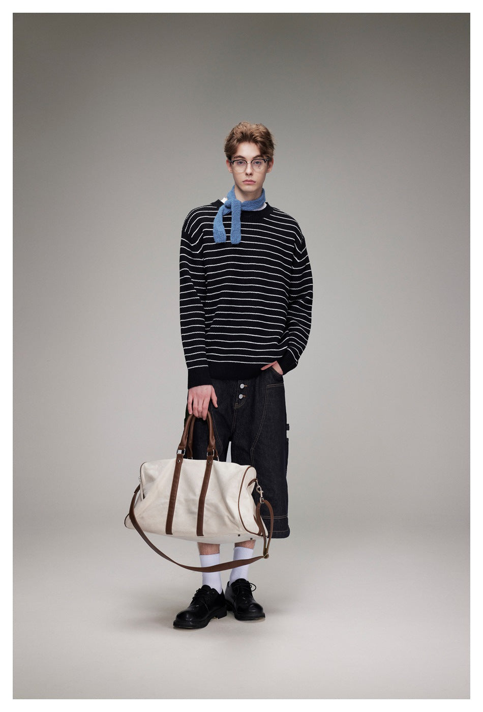 Full-length front view of a model in a black sweater with white stripes, blue scarf, and dark denim shorts.