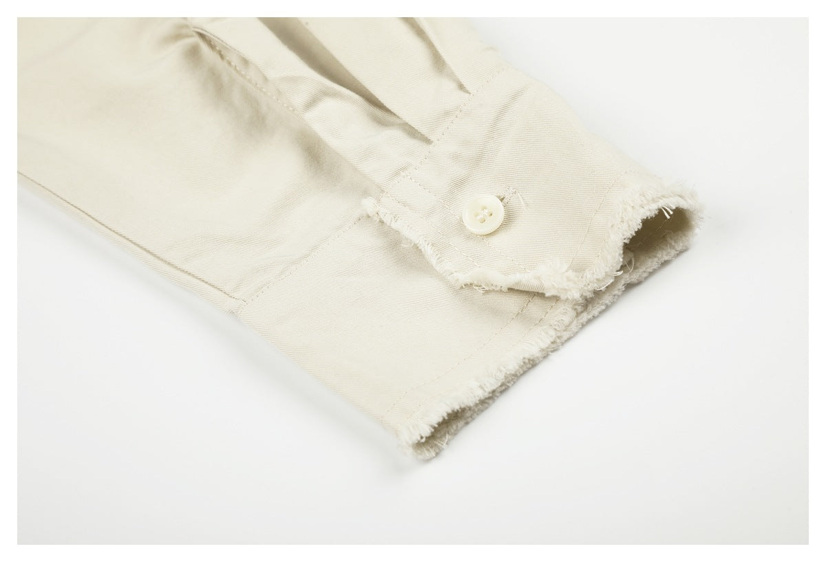 Close-up of an ivory shirt sleeve cuff with a button and frayed edges.