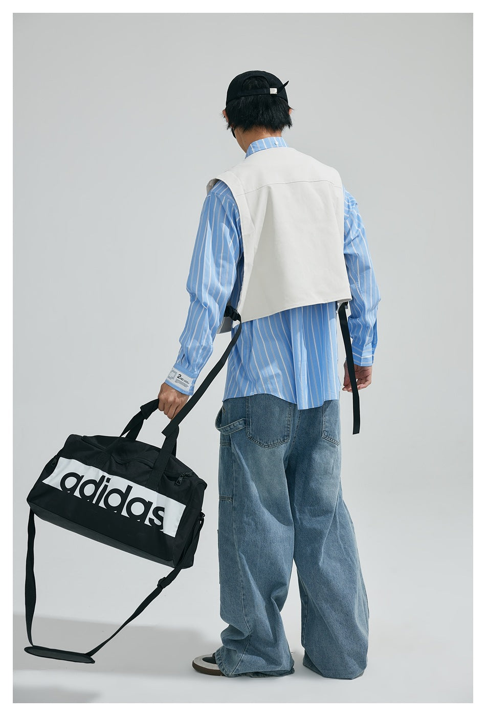 Rear view of a model wearing a white utility vest over a blue striped shirt and loose jeans.
