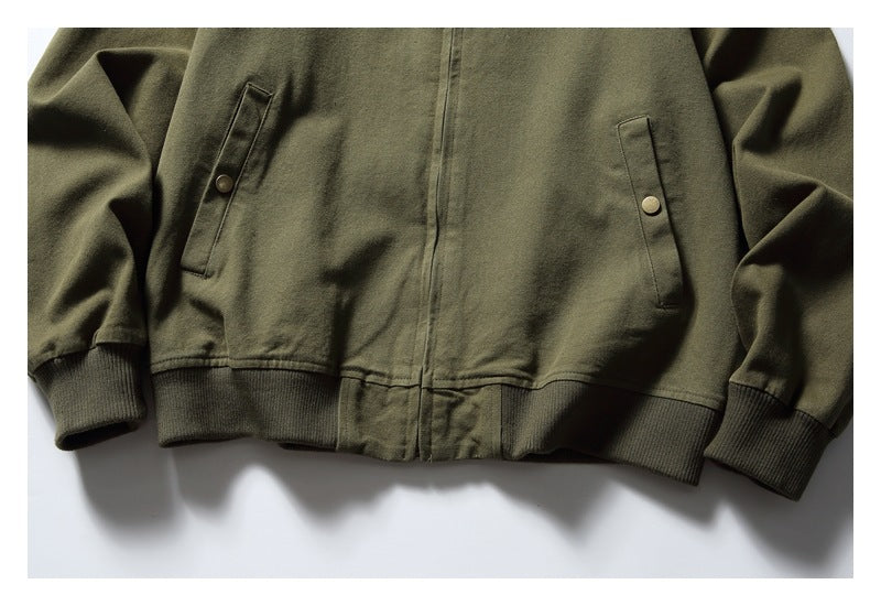 Lower front of an olive jacket with a center zipper, two snap-tab pockets, and ribbed cuffs and hem.