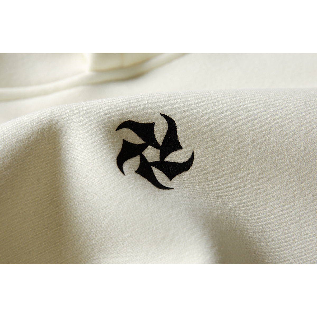Close-up of a small black abstract emblem printed on ivory hoodie fabric.