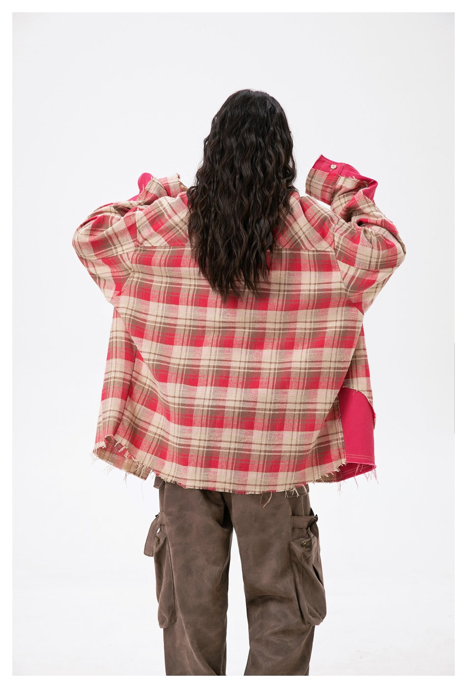 Rear view of a model in an oversized beige and red plaid shirt with a bright pink side panel and frayed hem.