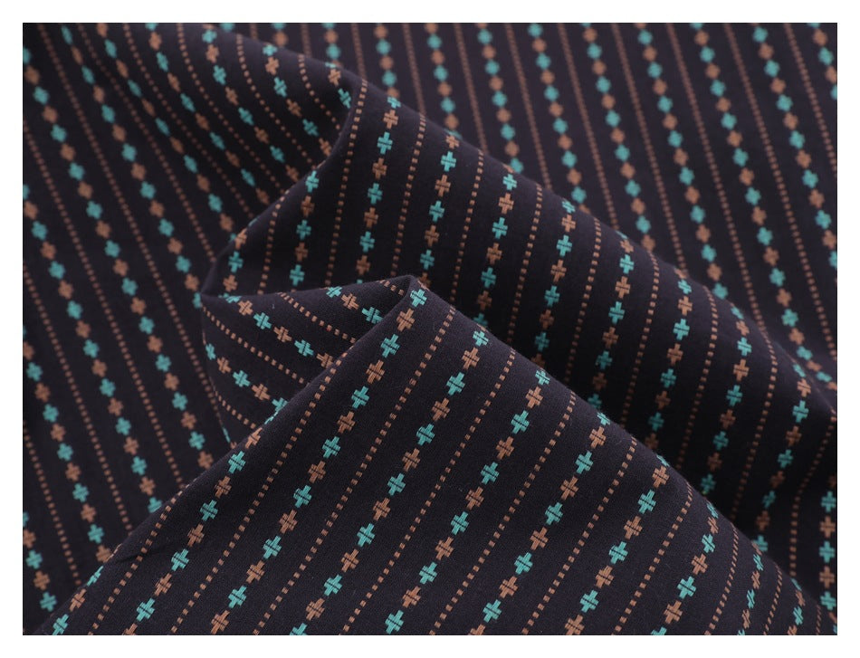 Close-up of dark fabric with vertical rows of teal and rust cross motifs and dotted lines.