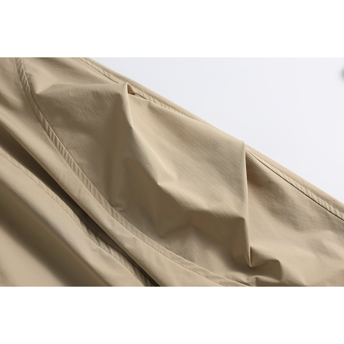 Close-up of tan pants showing a curved pocket opening, stitching, and folded fabric.