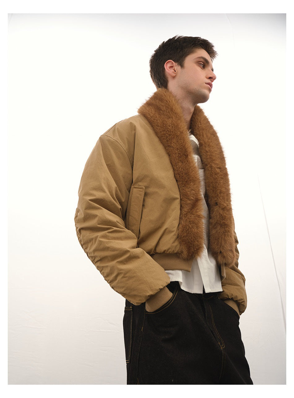 Man wearing a khaki cropped jacket with brown faux-fur collar over a white shirt and dark jeans, low-angle view