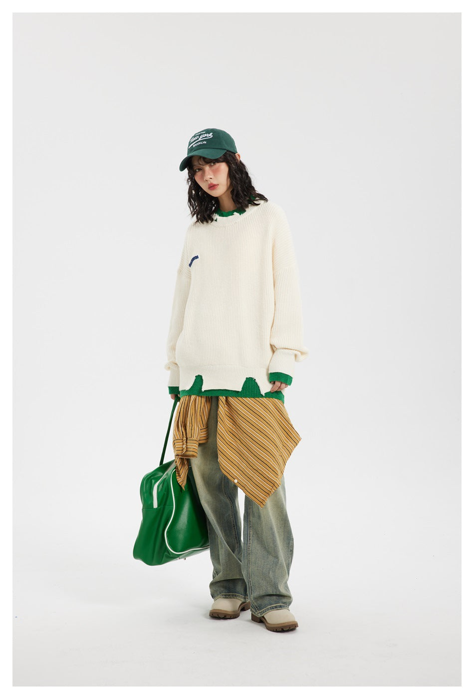 Model wearing off-white green-trim distressed sweater with green cap, striped shirt tied at waist, jeans and green bag