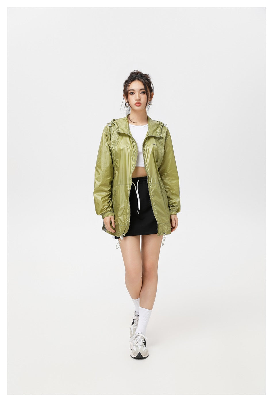 Model wearing an open olive-green hooded jacket over a white top and black skirt.