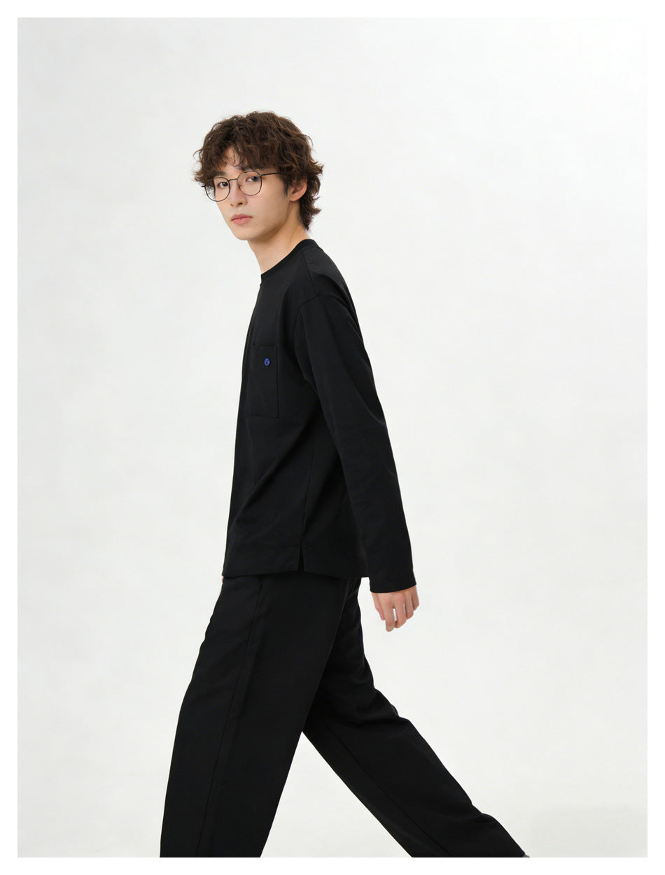 Model in black long-sleeve crew neck top with chest pocket and black wide trousers, side view walking