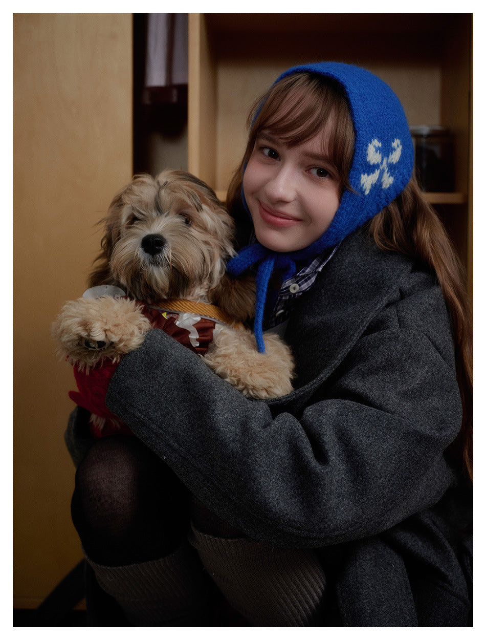 Close-up of a model in a charcoal gray coat and bright blue patterned bonnet, holding a small dog.