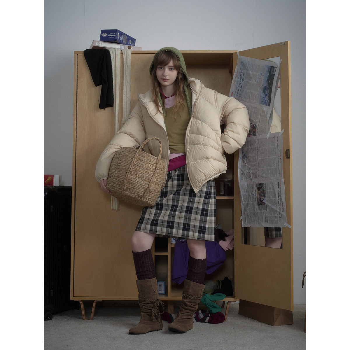Model wearing a cream oversized puffer jacket with a plaid skirt and carrying a woven bag.