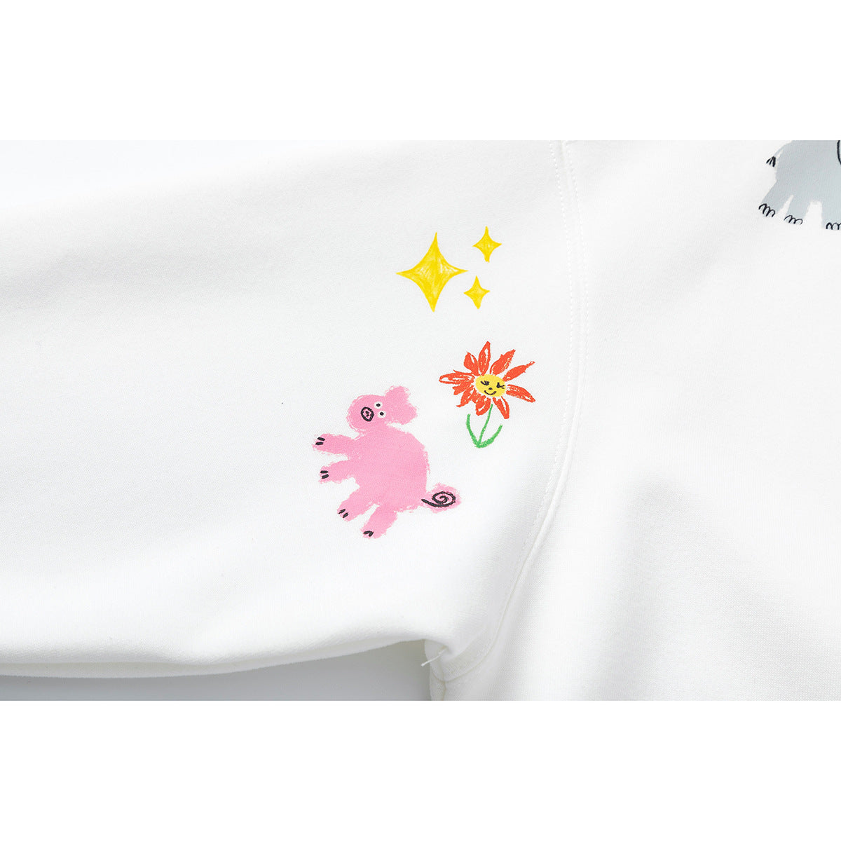 Close-up of a white sweatshirt sleeve with a pink cartoon animal, an orange flower, and yellow stars.
