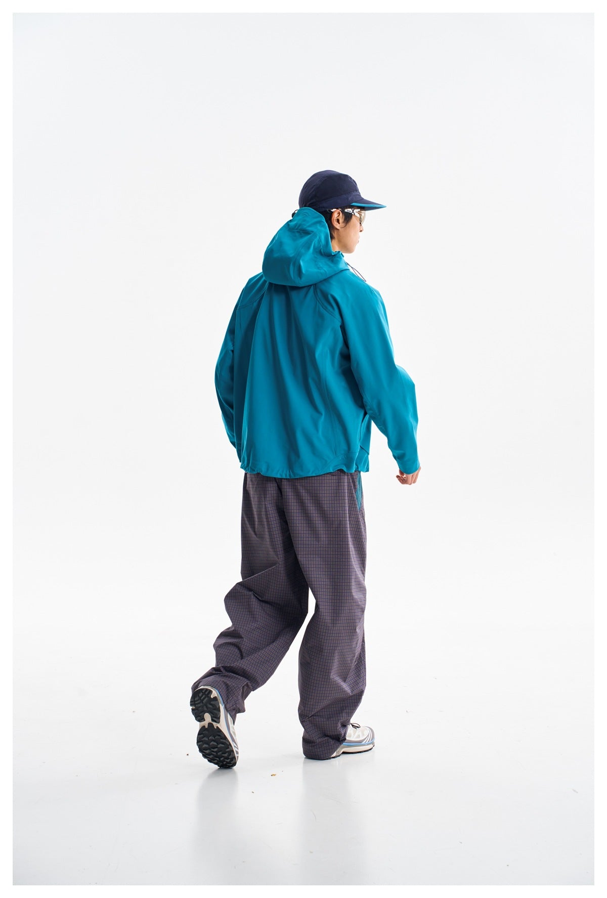 Model wearing the teal hooded jacket, shown from behind with loose plaid trousers.
