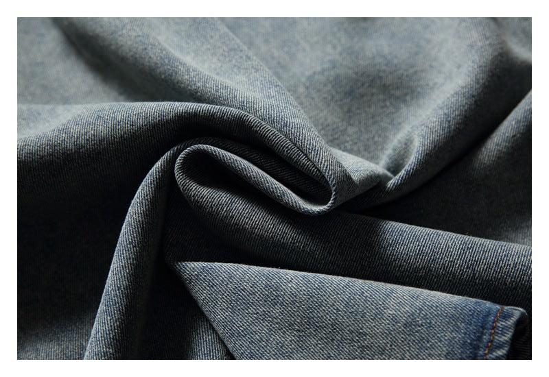 Close-up of faded blue denim fabric gathered into soft folds, with a stitched edge visible.