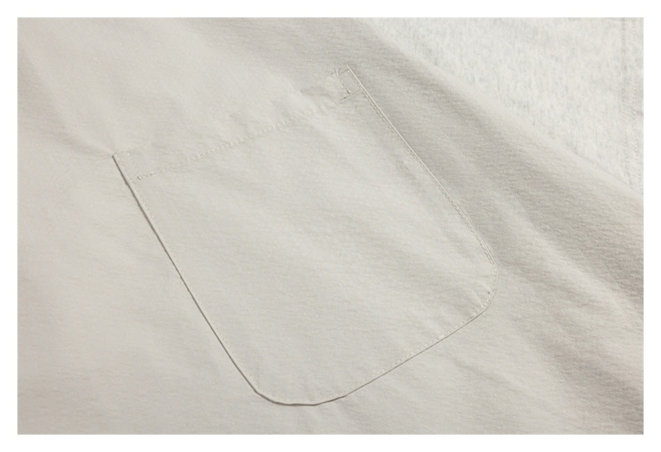 Close-up of a large stitched patch pocket on an off-white garment.