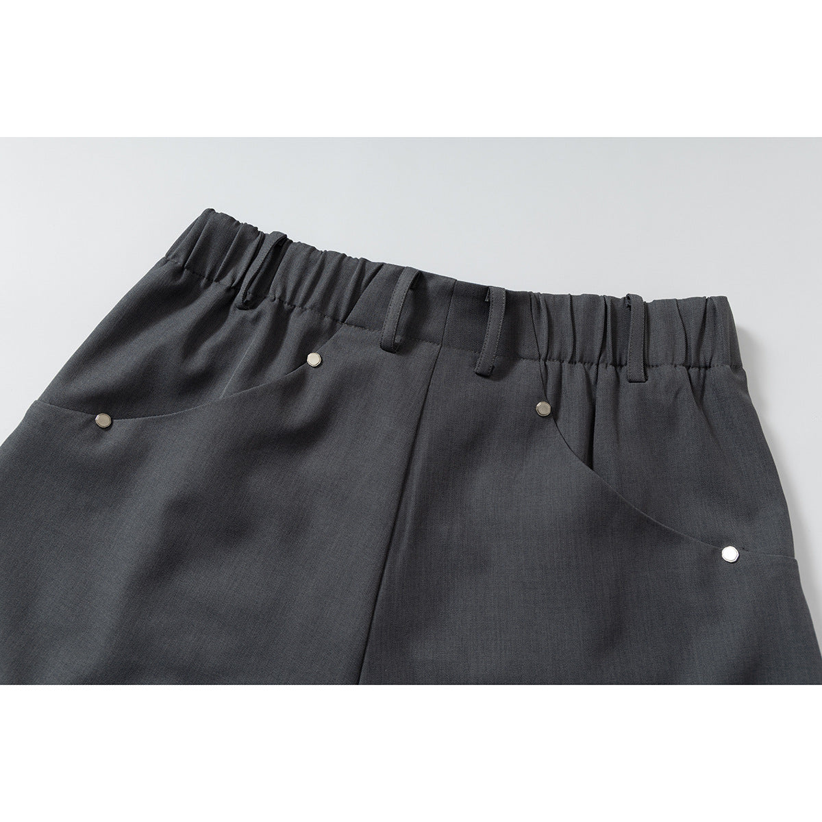Close-up of charcoal gray shorts showing an elasticized waistband, belt loops and curved front pockets with metal rivets.