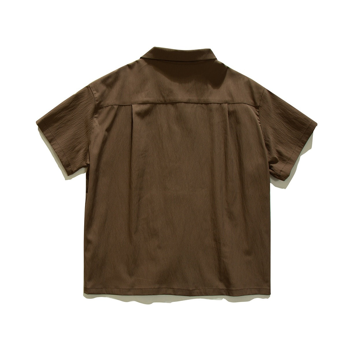 Back view of a brown short-sleeve collared shirt laid flat, with a back yoke and pleat.