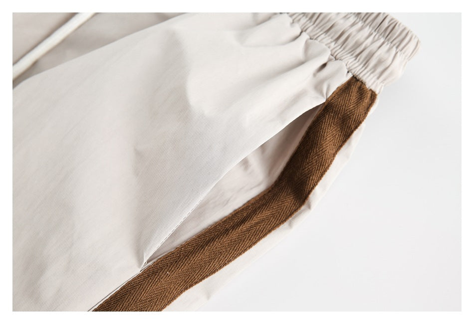 Close-up of beige pants showing a wide brown textured stripe along the side seam.