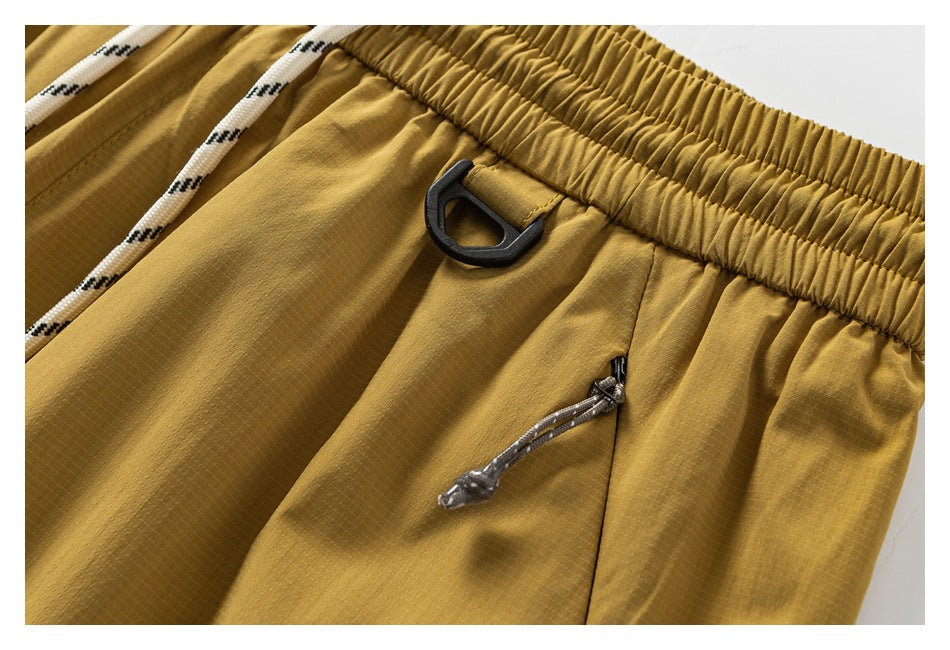 Close-up of mustard pants showing the waistband, black loop detail, and zip pocket.