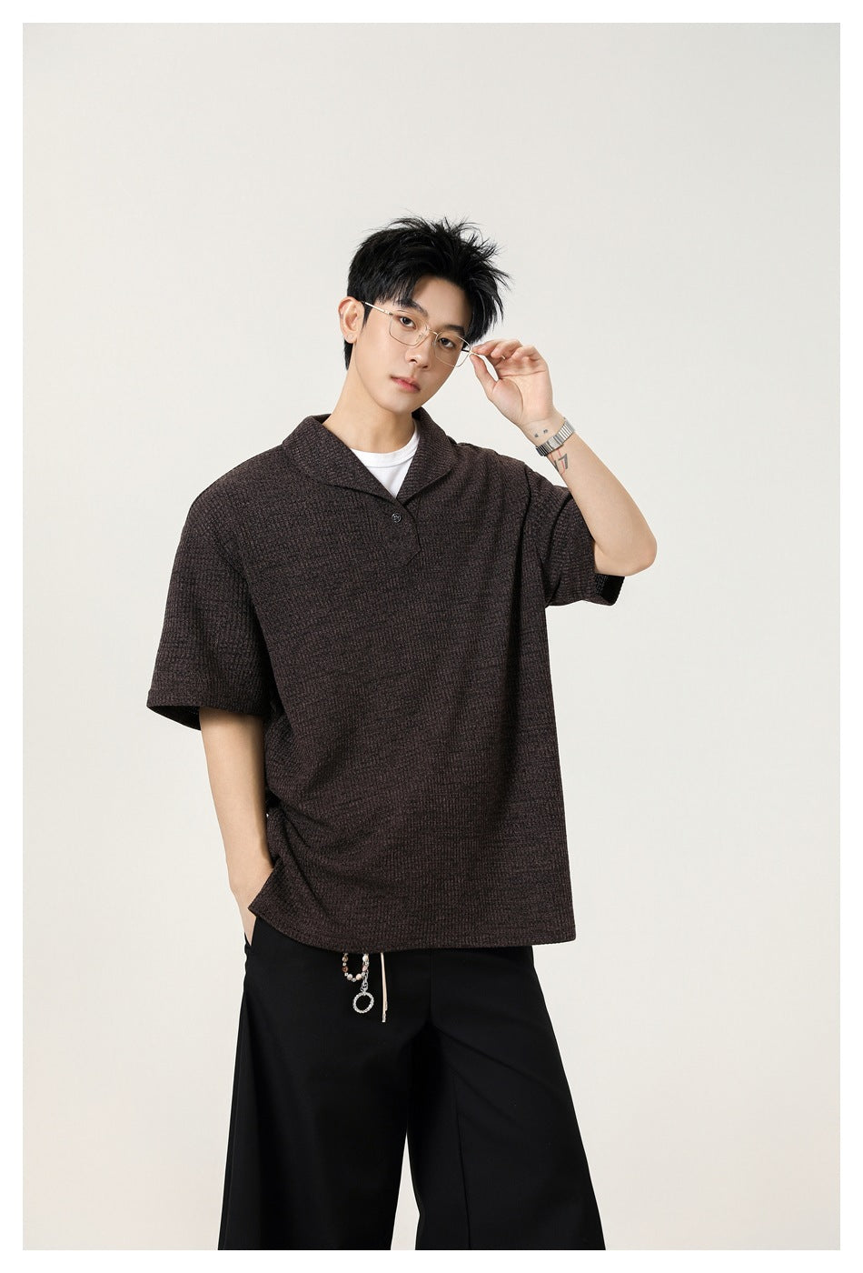 Model in coffee brown textured short-sleeve shawl-collar top and black trousers, adjusting glasses