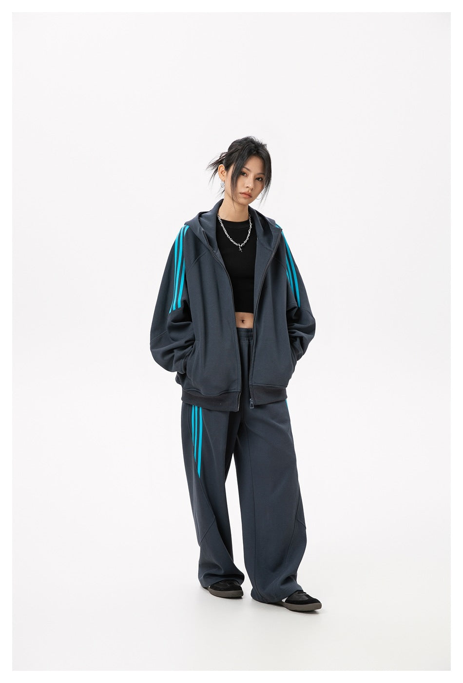 Full-length model in a charcoal zip-up hoodie and matching loose pants with bright cyan stripes.