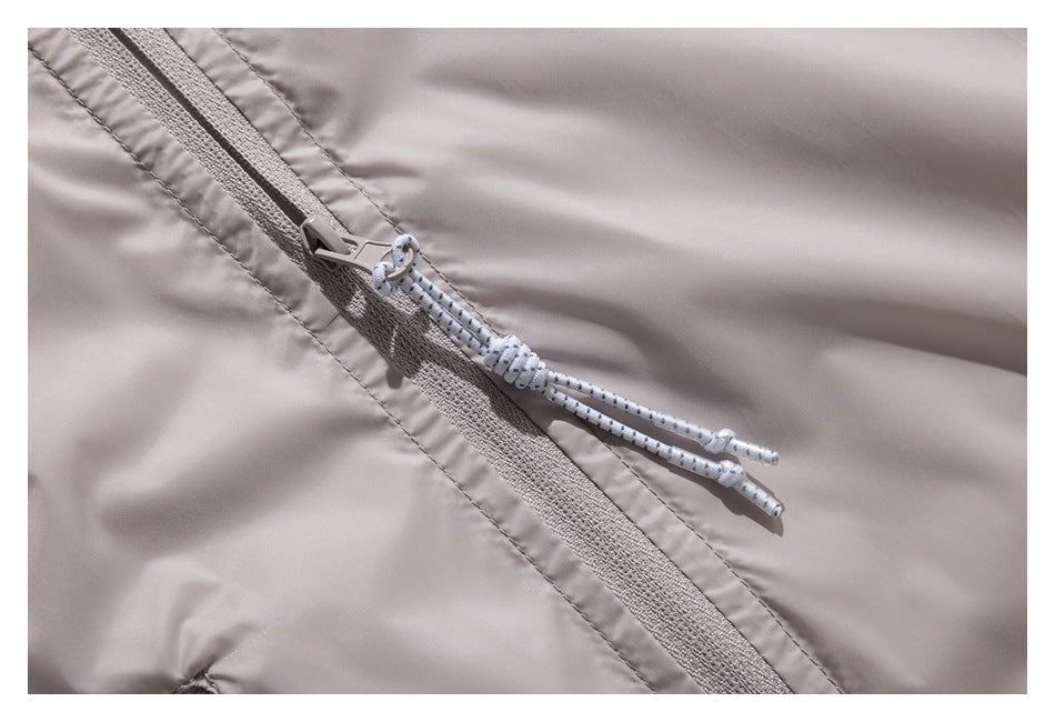 Close-up of a pale jacket zipper with white cord pulls on light taupe fabric.