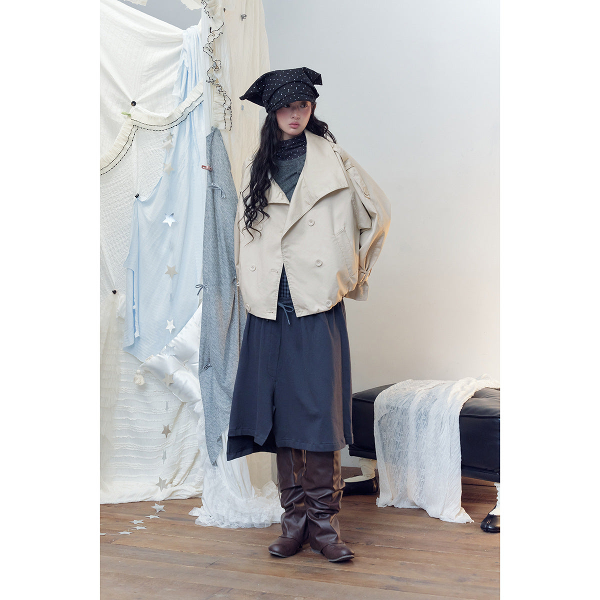 Model wearing a cropped cream double-breasted jacket with wide lapels, styled with navy bottoms and a black polka-dot hat.
