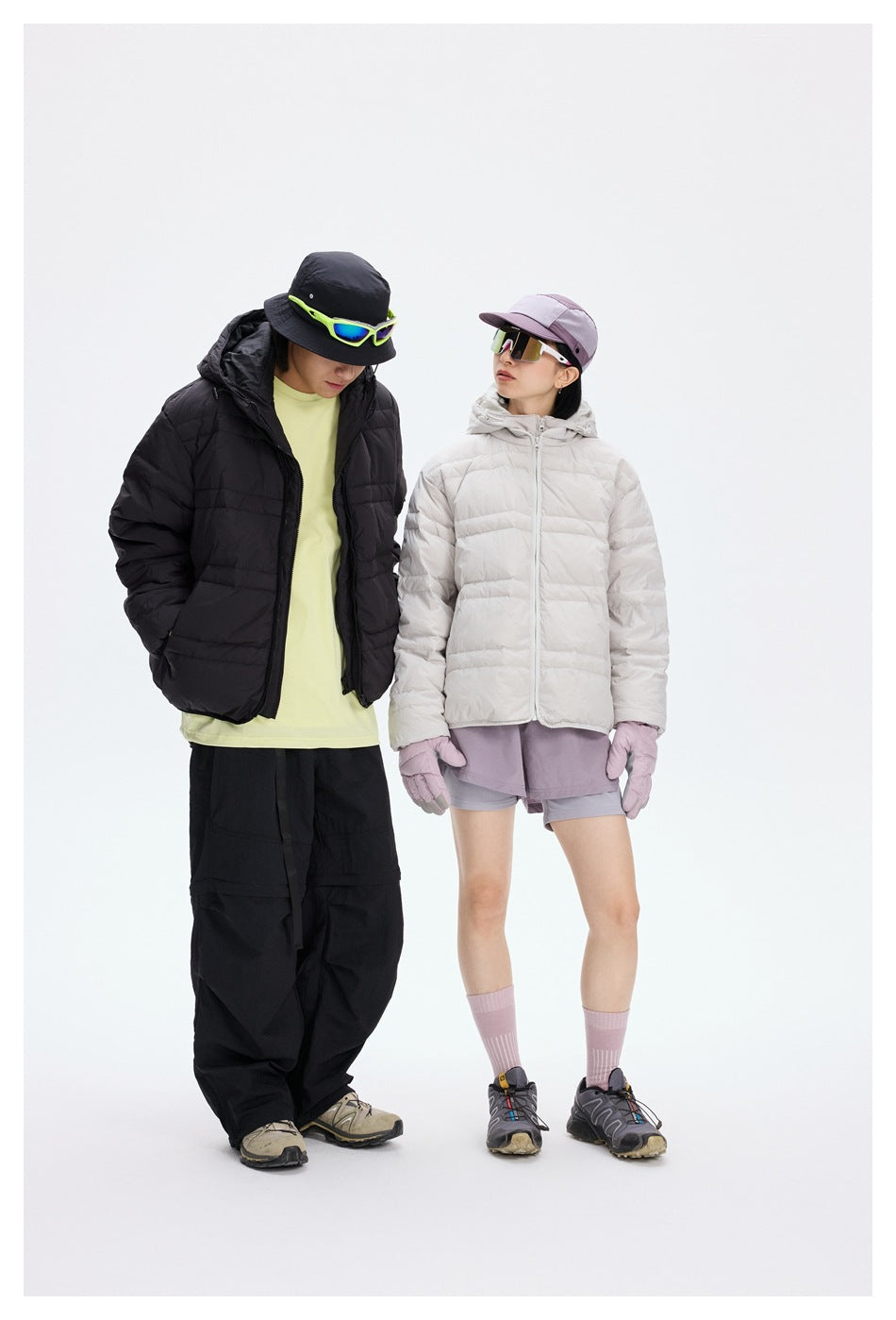 Two models wearing black and light gray quilted hooded jackets with outdoor-style hats, gloves and sunglasses.