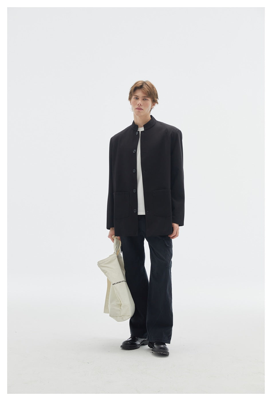 Full-length model wearing a black button-front jacket with two front patch pockets and loose black trousers.