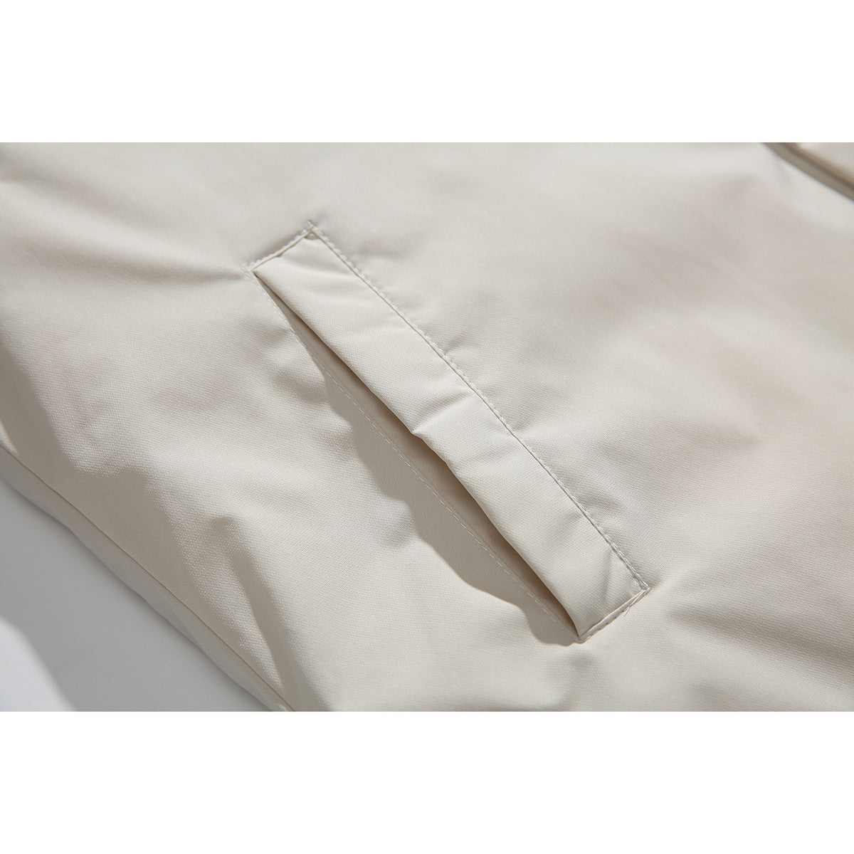 Close-up of a stitched pocket opening on the ivory shirt jacket.