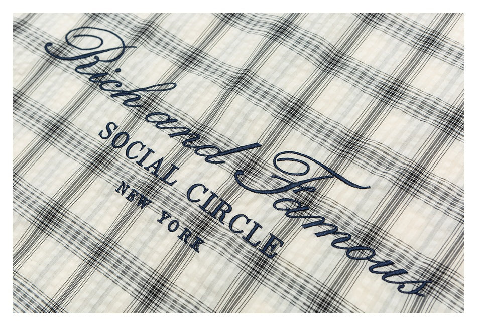 Navy embroidered lettering on cream-and-black plaid fabric.