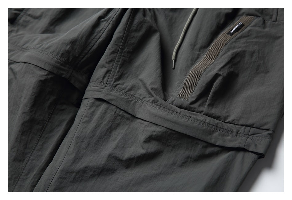 Close-up of charcoal pants showing a large flap pocket and narrow woven trim.
