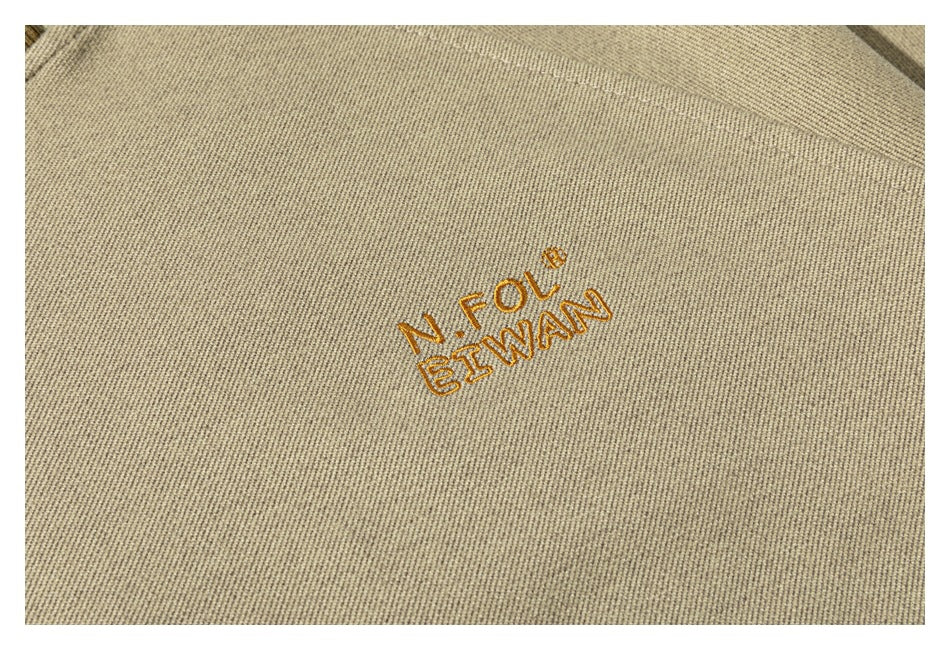Close-up of gold embroidered lettering on beige sweatshirt fabric.