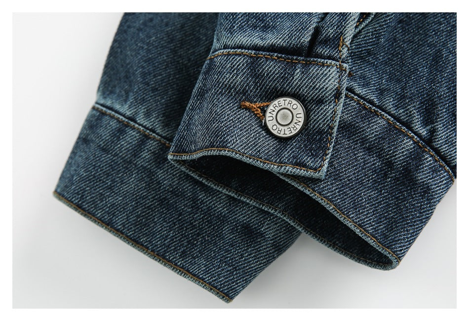 Close-up of a dark blue denim jacket cuff with a metal button and tan stitching.