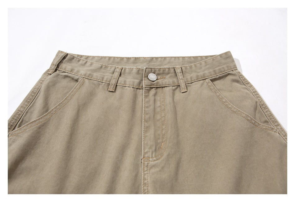 Close-up of the front waistband and angled pockets of taupe pants, showing the button, belt loops, and fly stitching.