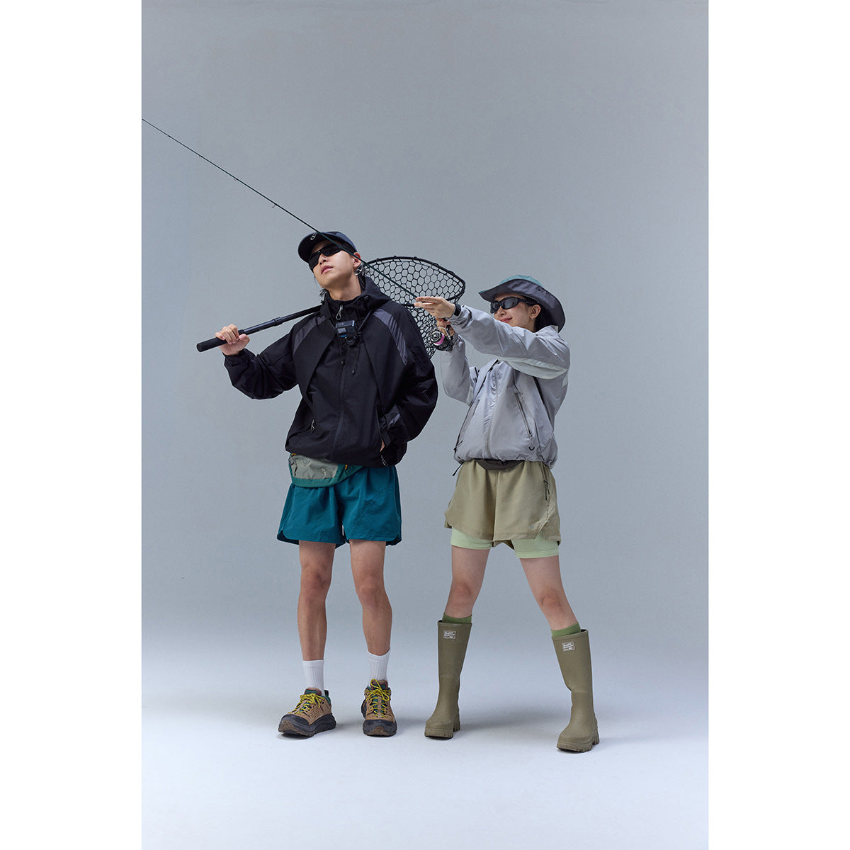 Two anglers model a black jacket and a light gray jacket with outdoor shorts while fishing.