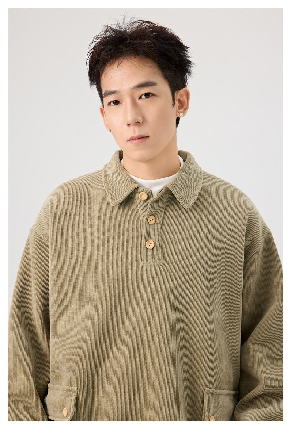 Close-up front view of a model wearing an olive pullover with a ribbed texture, pointed collar and wooden-look buttons.