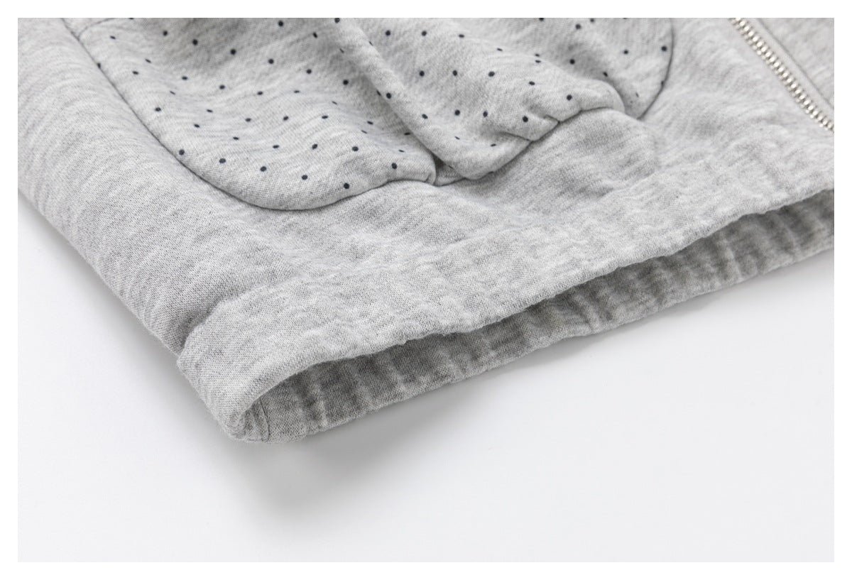 Close-up of the folded hem and dotted pocket area of a light gray garment.