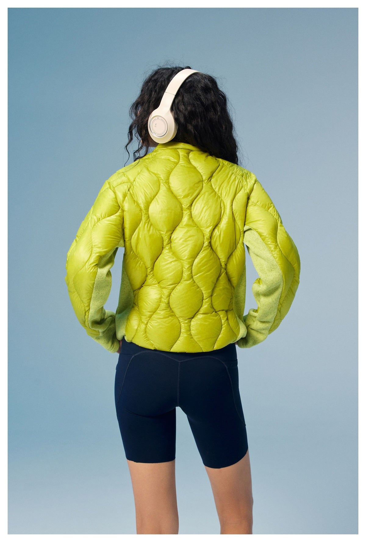 Rear view of a model wearing a lime-green quilted jacket with contrasting sleeves.