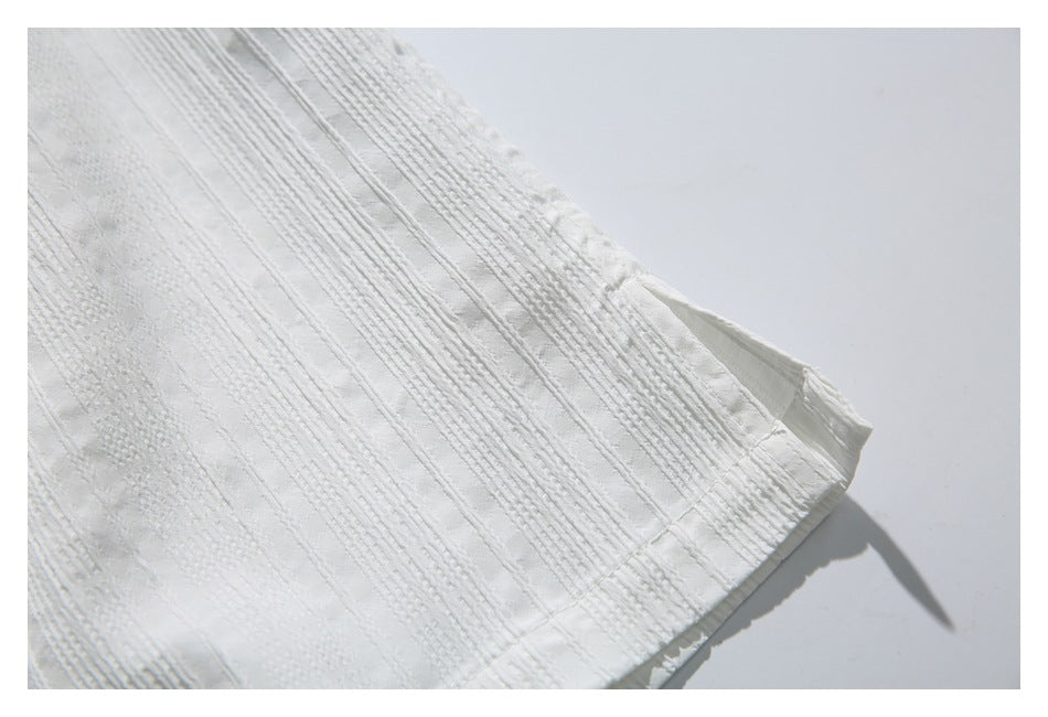 Close-up of the white shirt's textured fabric and finished lower hem.