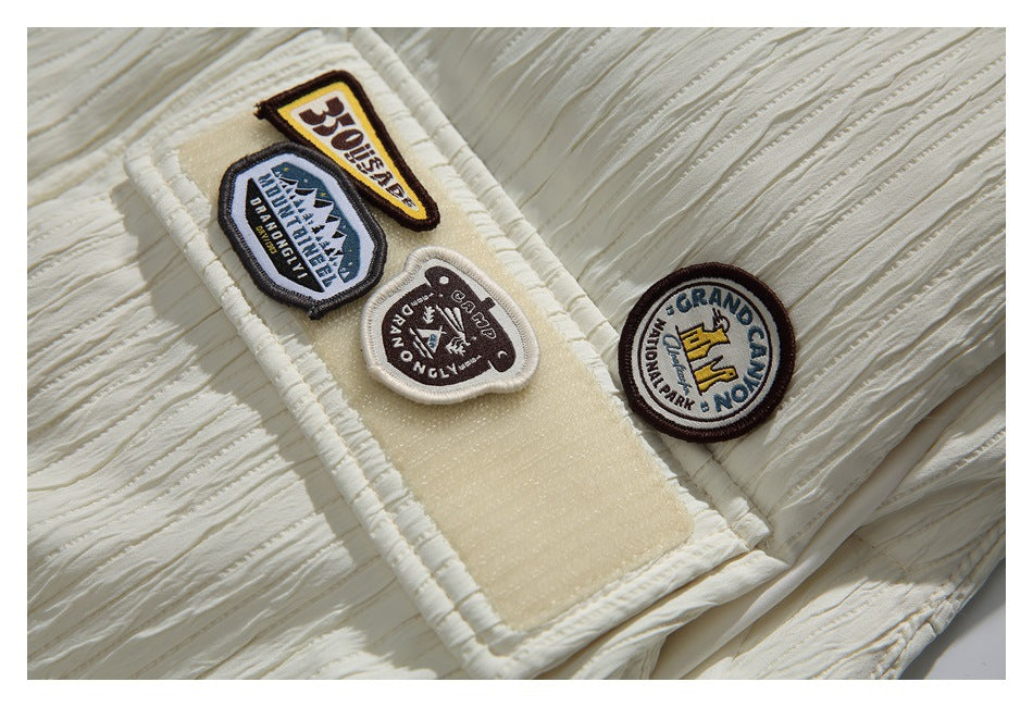 Close-up of a cream garment with several embroidered badge patches and gathered, textured stitching.