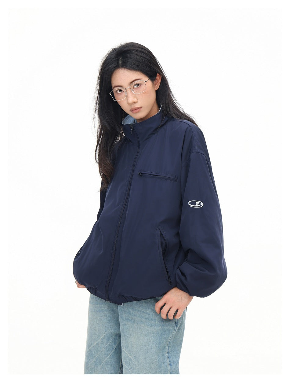 Angled view of a model wearing a navy jacket with a stand collar, zip pockets and a small white sleeve emblem.