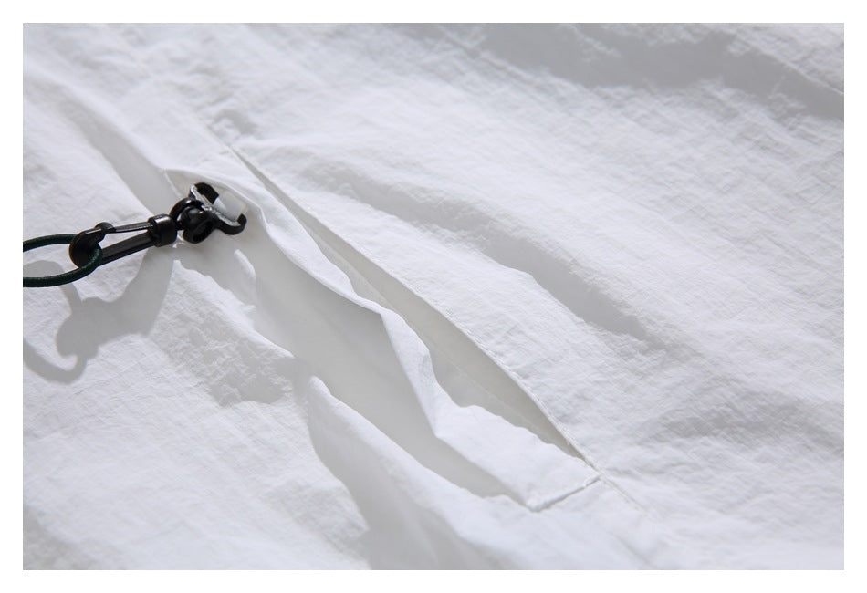 Close-up of white crinkled garment fabric with a black drawcord toggle and gathered seam.