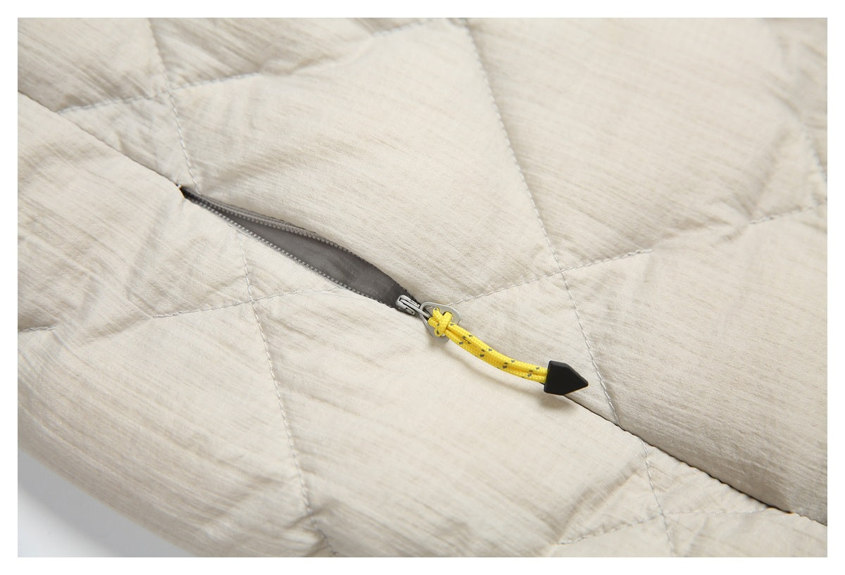 Close-up of a zip pocket on the cream quilted jacket, with a yellow cord pull and black tip.