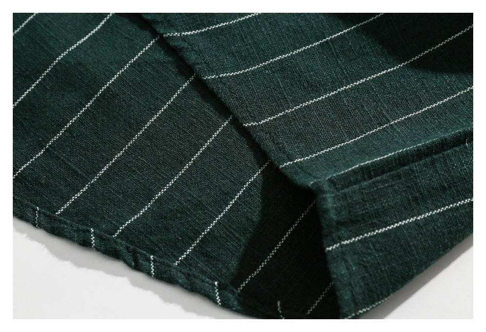 Close-up of the hem and stitched edge of dark green fabric with thin white stripes.