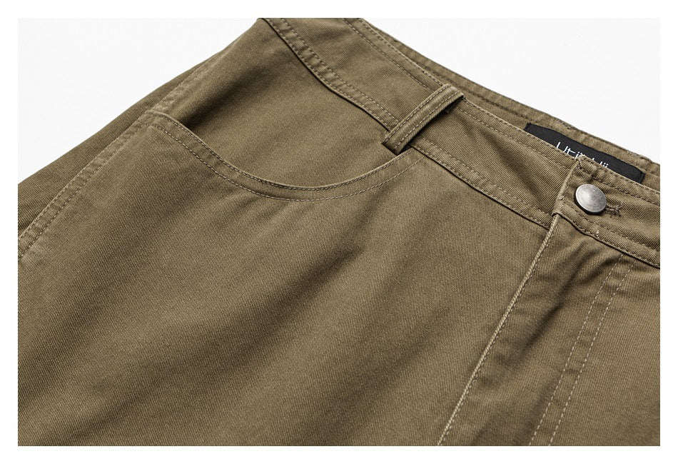 Close-up of brown trousers showing a curved front pocket, belt loop, waistband, and button.