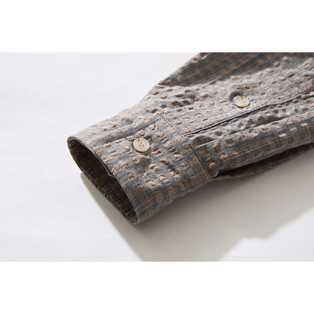 Close-up of the gray-brown textured plaid shirt sleeve cuff with two light buttons.