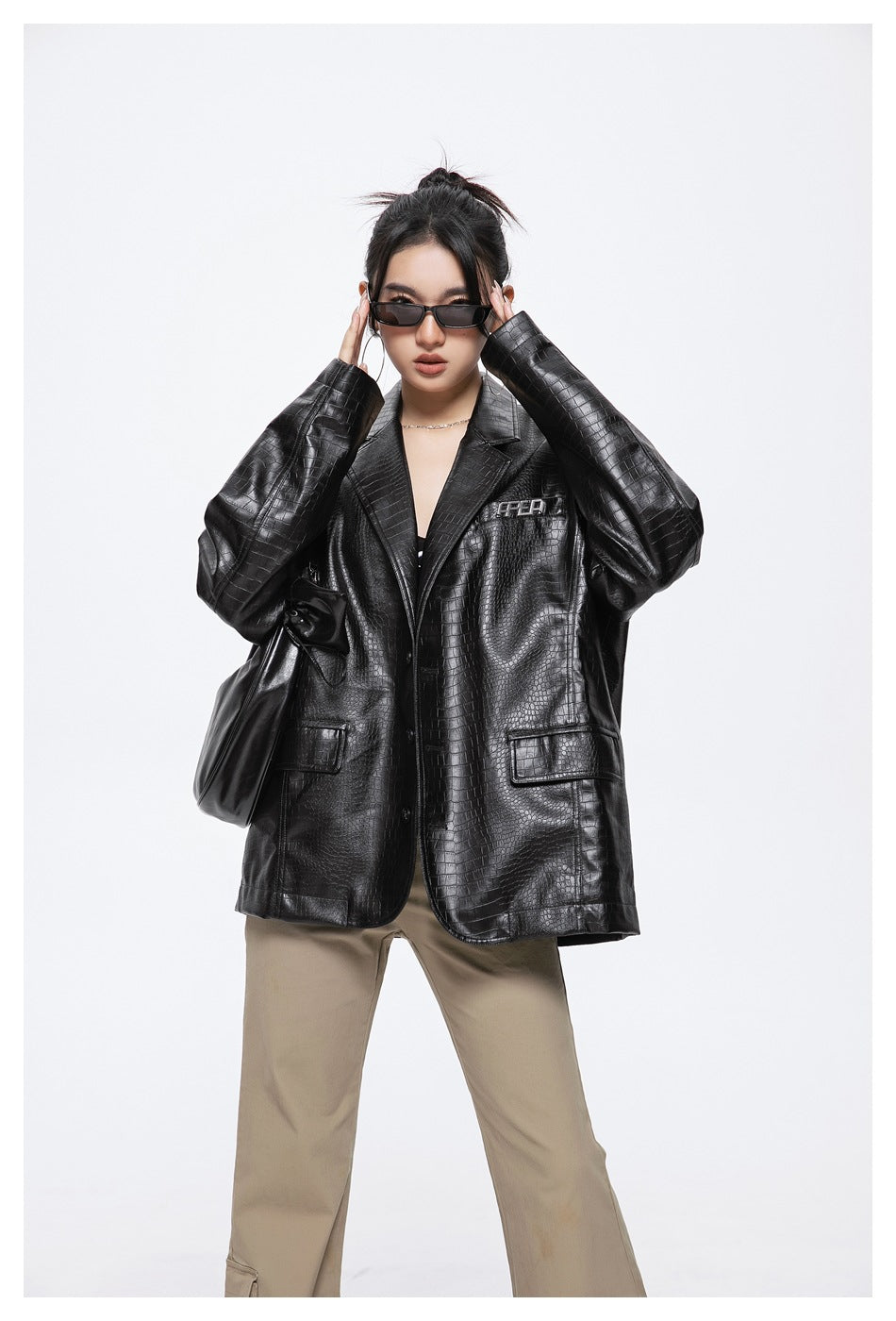 Model wearing a black crocodile-embossed oversized blazer with beige trousers and sunglasses.