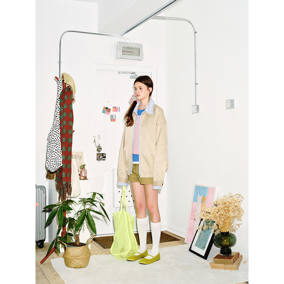 Model in a beige zip jacket with a blue striped collar and cuffs, olive shorts, and a bright yellow tote.