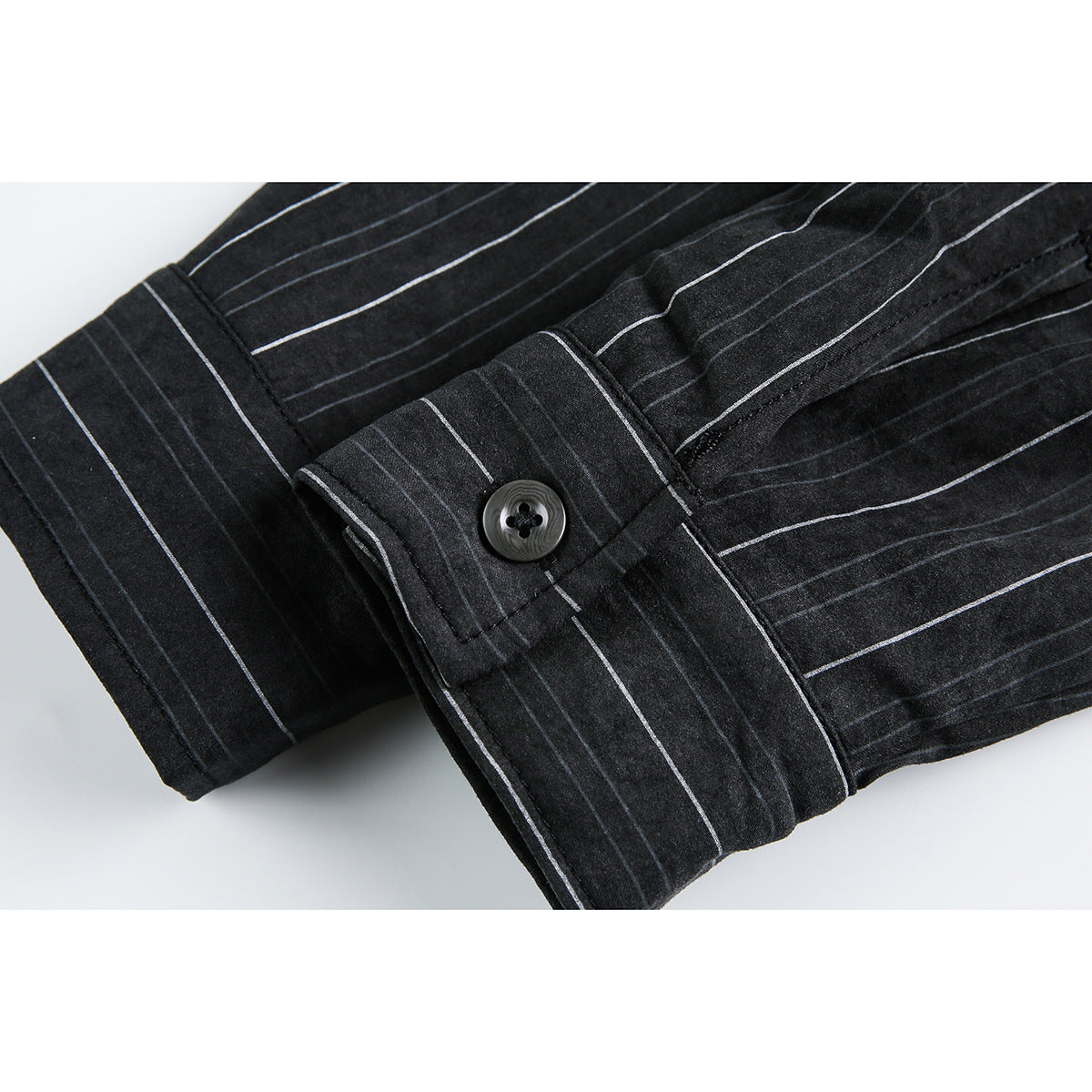 Close-up of a black shirt cuff with a button and thin light vertical stripes.